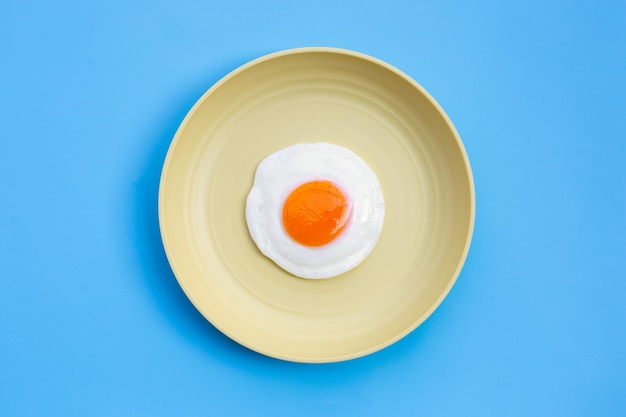 Œuf frit dans un plat jaune sur fond bleu. Vue de dessus