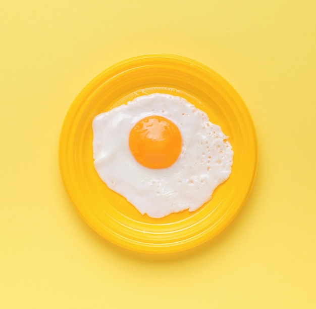 Œuf frit sur une plaque jaune sur fond jaune Concept minimal Un petit-déjeuner populaire
