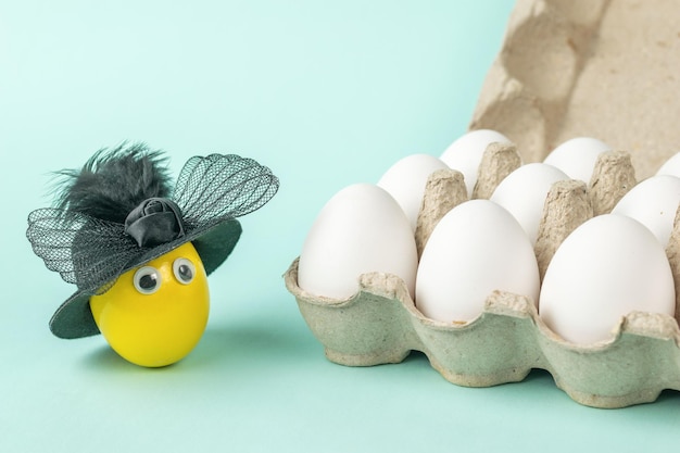 Un œuf jaune dans un chapeau près d'une boîte d'œufs ordinaires.