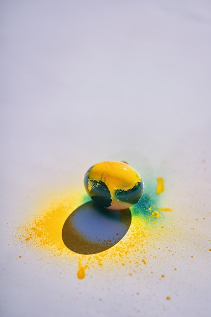 Un œuf jaune avec de la peinture bleue et jaune se trouve sur une surface blanche.