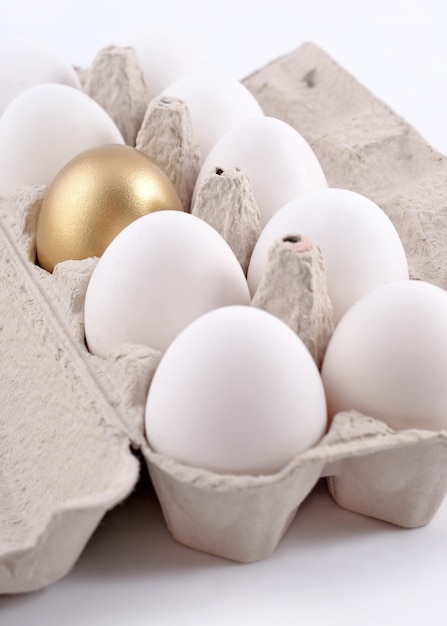 Oeuf d'or et œufs dans une boîte en carton sur fond blanc