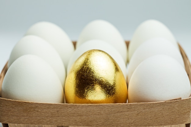 Un œuf d'or parmi les œufs blancs dans une boîte en bois