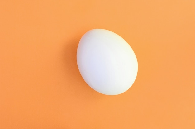 Un oeuf de Pâques blanc sur un fond orange vif