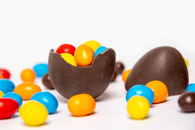 Oeuf de Pâques en chocolat cassé avec des décorations de bonbons colorés sur fond blanc avec des bonbons colorés libre de la tradition de Pâques douce