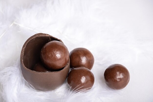 Oeuf de pâques en chocolat fêlé avec de petits bonbons ronds au chocolat dans un nid de plumes blanches copie espace friandise au chocolat pour les enfants concept de Pâques