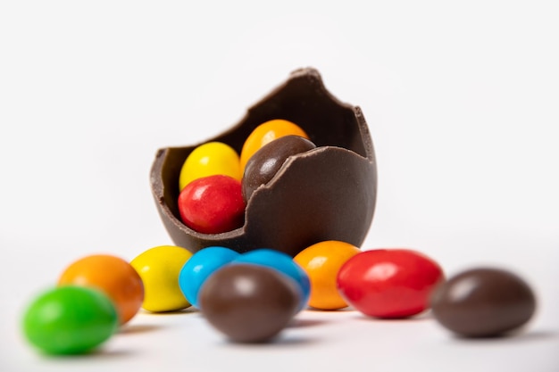 Oeuf de Pâques en chocolat fêlé plein de petits bonbons ronds colorés sur fond blanc avec des bonbons colorés en gros plan Gâterie au chocolat pour les enfants Concept de Pâques