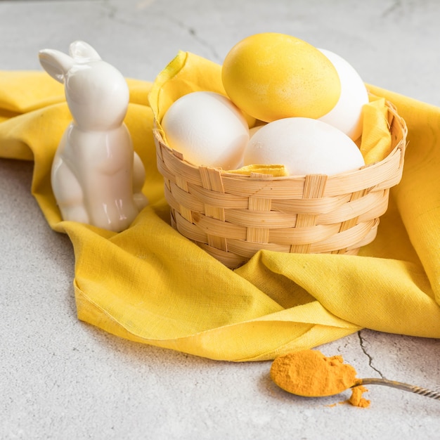 Oeuf de Pâques coloré et oeufs blancs dans un panier sur un tissu jaune