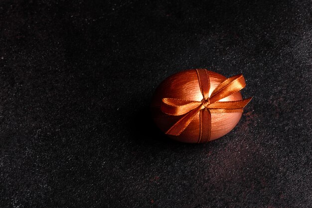 Oeuf de Pâques avec du ruban cadeau sur une table en bois sombre. Préparation pour les vacances