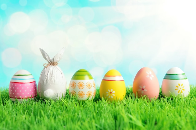 Oeuf de Pâques enveloppé dans un papier en forme de lapin avec des oeufs de Pâques colorés sur l'herbe verte.