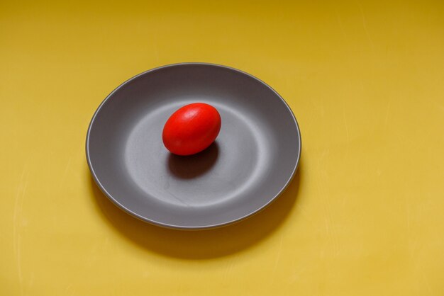 Oeuf de Pâques peint traditionnel coloré. Oeuf rouge, fond jaune. oeuf dans une assiette grise