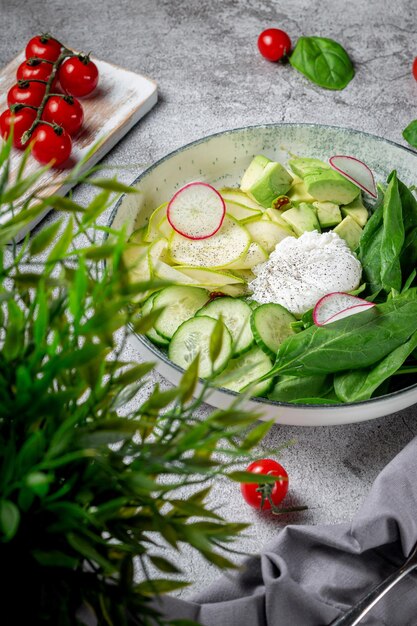 Oeuf poché. Salade verte avec avocat, concombre, feuilles d'épinards, courgettes et radis dans une assiette sur une table en pierre grise. Menu du restaurant