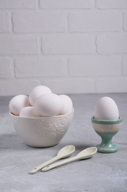 Oeuf de poule blanc dans un support en céramique et oeufs dans un bol blanc