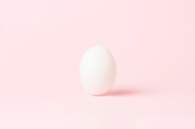 Oeuf de poulet blanc sur une surface rose. Le minimalisme. Vue de côté.