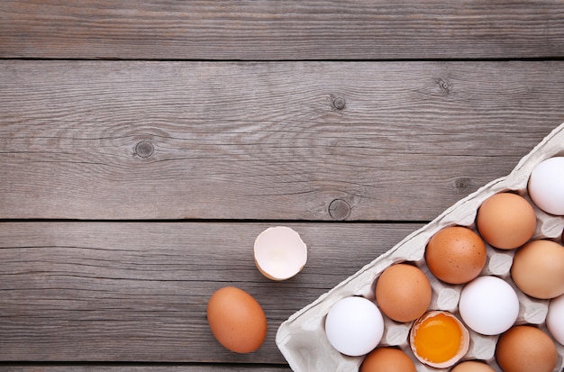 L'œuf de poulet est à moitié cassé parmi les autres œufs. Œufs de poule dans des conteneurs sur fond en bois gris