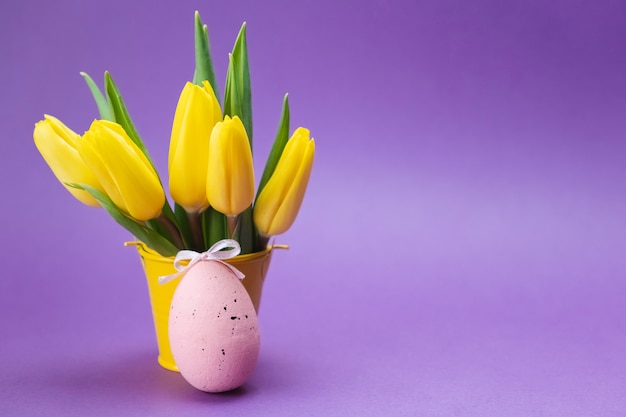 Oeuf rose et tulipes jaunes sur une surface violette