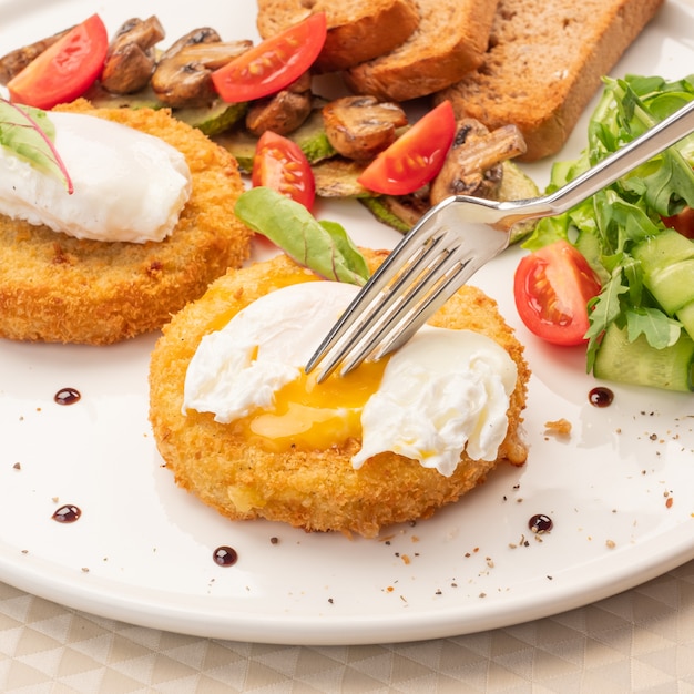 Des œufs de Benoît sur une assiette, une fourchette déchire un œuf et le jaune coule.