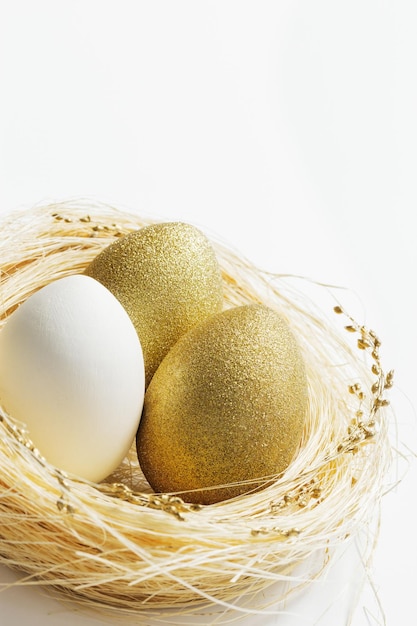 Photo des œufs blancs et dorés de pâques dans un nid de paille sur un fond blanc un œuf lumineux à la mode pour les vacances de printemps