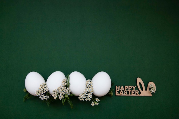 Oeufs blancs de Pâques festifs avec de petites fleurs blanches sur fond vert A proximité se trouve une inscription en bois Joyeuses Pâques