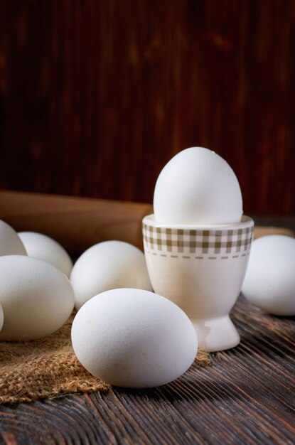 Oeufs blancs sur toile de jute et table en bois. En arrière-plan, un rouleau à pâtisserie rustique. Discret.