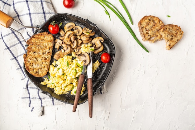 Oeufs brouillés aux champignons dans une casserole sur un tableau blanc. petit-déjeuner ou brunch santé. Repas fait maison, vue de dessus, mise à plat.