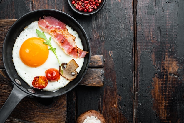 Oeufs brouillés dans une poêle avec du saindoux de porc, du pain et des plumes vertes dans une poêle en fonte, sur le vieux fond de table en bois sombre, vue de dessus à plat,