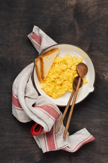 Oeufs brouillés pour le petit déjeuner sur une vieille poêle à frire rouge, mur de table en bois foncé. Petit-déjeuner anglais traditionnel. Vue de dessus avec espace pour faire face.