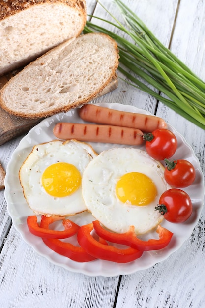 Oeufs brouillés avec saucisse et légumes servis sur assiette sur fond de bois