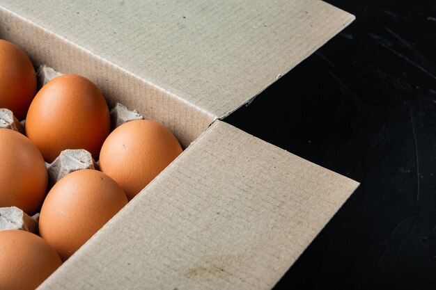 Oeufs bruns dans un plateau de boîte en carton, sur fond noir, avec un espace pour copyspace de texte