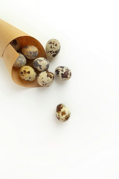 Oeufs de caille dans du papier d'emballage artisanal brun sur fond blanc Concept de Pâques créatif