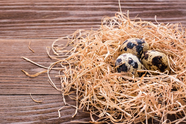 Oeufs de caille sur un tas de paille sur une table en bois