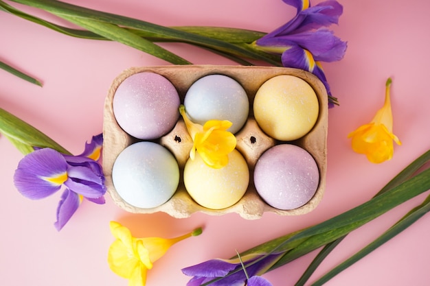 Oeufs colorés de Pâques dans un plateau à oeufs avec des fleurs sur une surface jaune. Mise à plat.