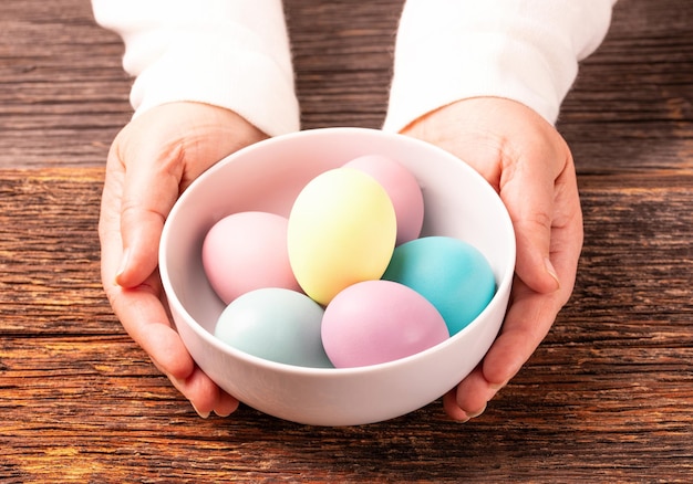 Oeufs colorés teints de pâques élégants sur une plaque blanche fond rustique en bois mains de femme