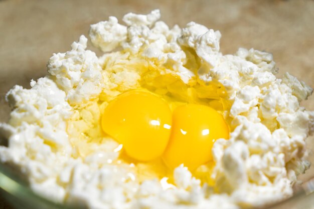 Oeufs crus avec du fromage cottage dans un bol Préparation de gâteaux au fromage