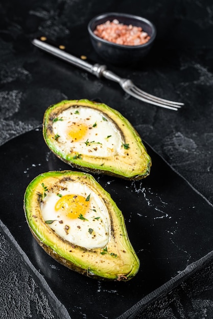 Oeufs cuits à l'avocat avec herbes et épices Fond noir Vue de dessus