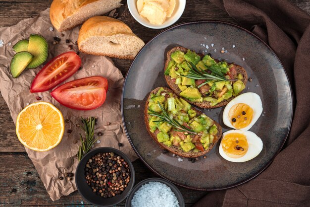 Oeufs durs et pain grillé avec avocat, tomate et romarin sur un fond en bois La vue du haut. Le concept d'une bonne nutrition.