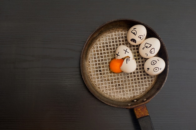 Oeufs avec les émotions dessinées, oeuf cassé au centre de la casserole, tableau noir