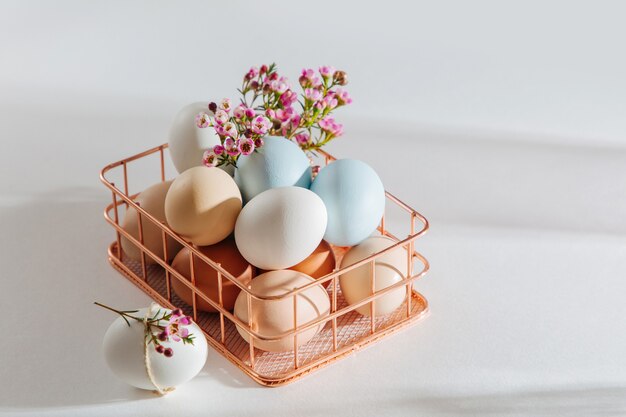 Oeufs et fleurs de couleur naturelle dans un panier avec des lumières du soleil. Compositions élégantes aux couleurs pastel. Notion de Pâques.