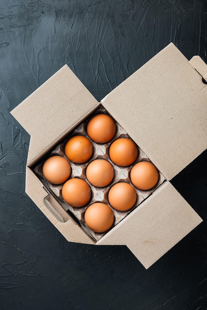 Oeufs frais sur un coffret d'oeufs en papier, sur fond noir, vue de dessus à plat