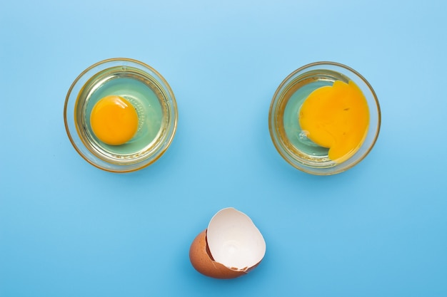 Photo oeufs frais crus dans un bol en verre avec coquille d'oeuf sur fond bleu. bon et pauvre jaune comparer