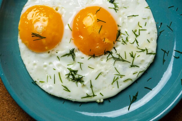 Oeufs frits sur une assiette turquoise saupoudrée d'aneth vue de dessus