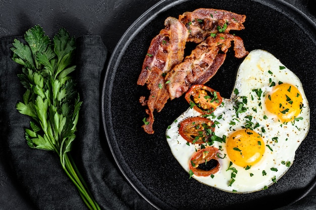 Oeufs frits au bacon. Petit déjeuner classique à l'hôtel. Fond noir. Vue de dessus