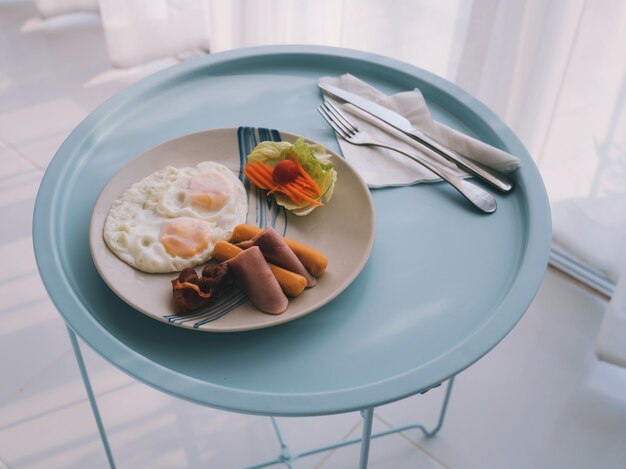 Oeufs frits, bacon et saucisses sur une petite table dans une chambre confortable pour une personne