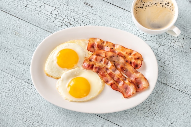 Oeufs frits avec des bandes de bacon sur la plaque blanche