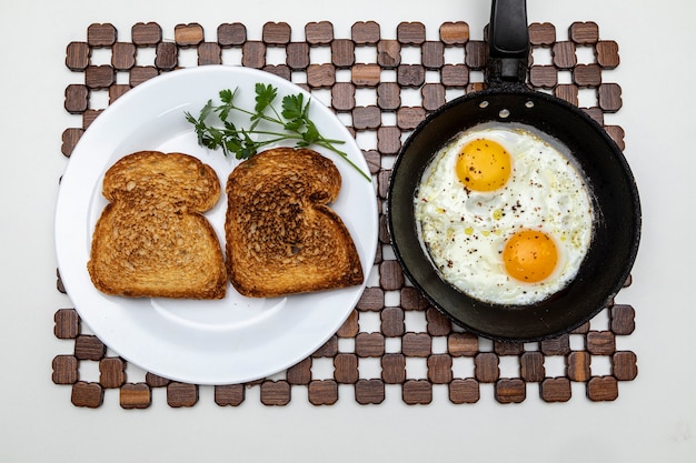 Oeufs frits dans une poêle en fer rustique, pain grillé sur un plat pour le petit déjeuner