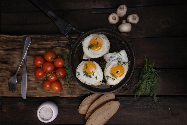 Des œufs frits avec du bacon et des légumes dans une poêle à frire en fonte sur un vieux fond de table en bois foncé