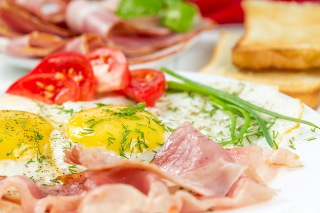 Œufs frits avec jambon et tomates sur une plaque blanche