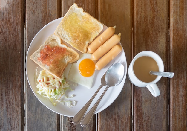 Photo Œufs frits, pain grillé avec confiture de fraises, saucisses, salade sur assiette blanche avec tasse à café