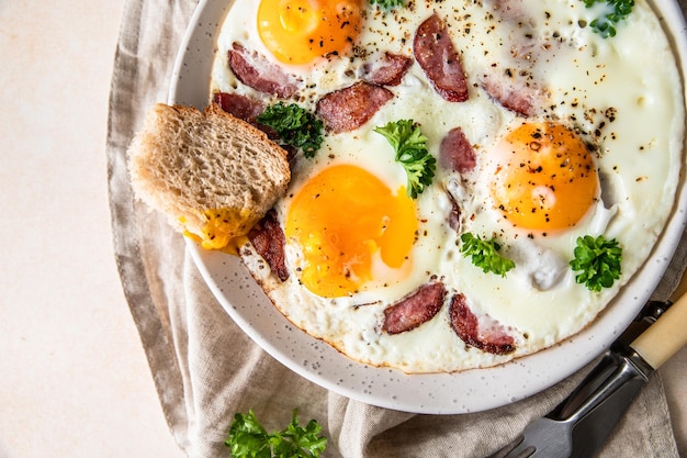 Oeufs frits avec saucisse et persil sur une assiette en céramique servis avec du pain