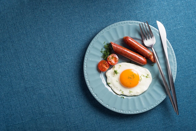 Oeufs frits saucisses de porc et tomates fraîches sur une nappe bleue