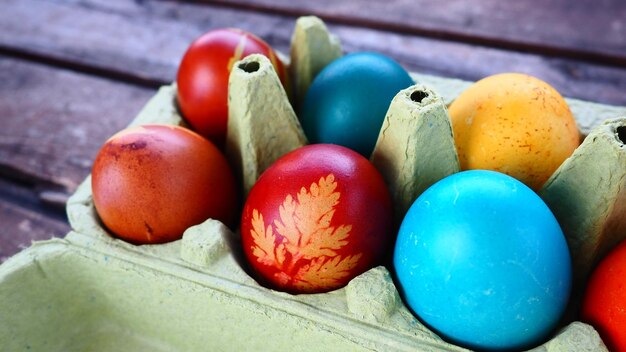 Oeufs multicolores peints à la gouache et à la pelure d'oignon dans une boîte en carton sur fond de table en bois Dix oeufs à la coque Affiche de carte postale pour Pâques Vacances de Pâques Oeufs bruns jaunes bleus rouges